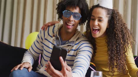 Video-of-happy-diverse-couple-celebrating-new-years-eve-and-making-video-call-on-smartphone-at-home