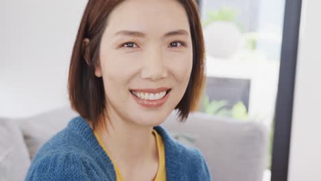 Video-portrait-of-happy-asian-woman-smiling-to-camera-sitting-at-home