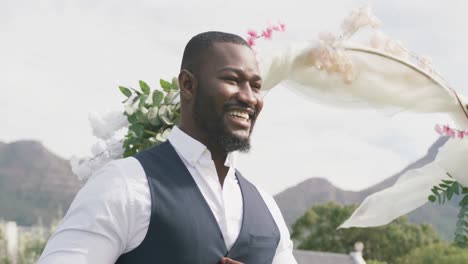 Video-Eines-Glücklichen-Afroamerikanischen-Bräutigams,-Der-Bei-Einer-Hochzeit-Im-Freien-Lächelt-Und-Spazieren-Geht