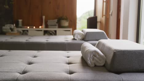 Vertical-video-of-massage-treatment-room-at-health-spa,-with-massage-tables-towels-and-lit-candles