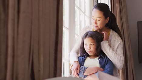 Video-of-thoughtful-asian-mother-and-daughter-looking-outside-window