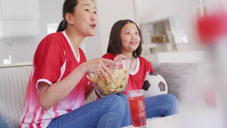 Video-De-Una-Feliz-Madre-Asiática-Y-Su-Hija-Comiendo-Papas-Fritas-Y-Viendo-Un-Partido-En-La-Televisión