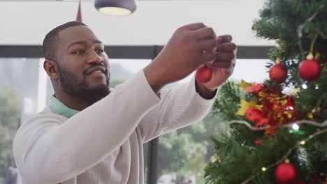 Video-of-happy-african-american-man-decorating-christmas-tree-at-home