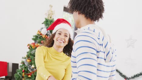 Video-Eines-Glücklichen,-Vielfältigen-Paares-Mit-Rentiergeweih-Und-Weihnachtsmütze,-Das-Zu-Hause-Am-Weihnachtsbaum-Tanzt