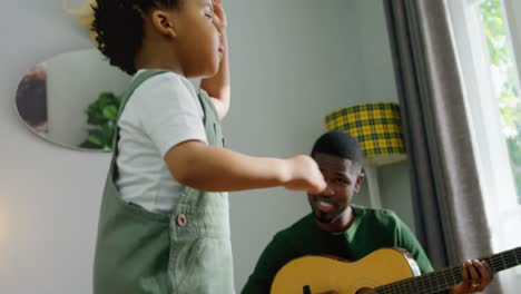 Animation-of-light-flashing-over-happy-african-american-father-and-son-playing-guitar