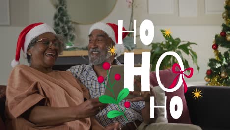 Animation-of-ho-ho-ho-text-over-senior-african-american-couple-wearing-santa-hats