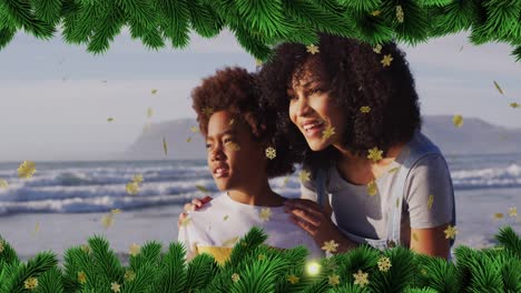 Animation-of-fir-tree-and-snowflakes-over-african-american-woman-and-her-son-at-beach