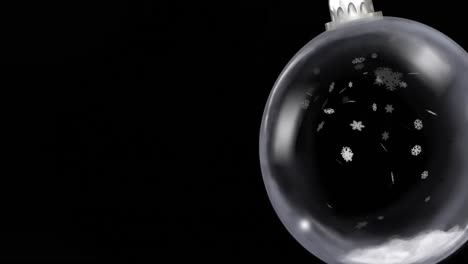 Animation-of-christmas-bauble-dangling-over-snow-falling-on-black-background