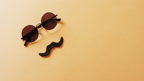 Video-of-false-moustache-and-round-sunglasses-on-yellow-background-with-copy-space