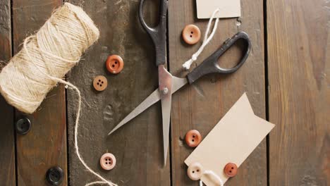 Video-of-scissors,-twine-string,-buttons-and-gift-tags-on-dark-wood-boards