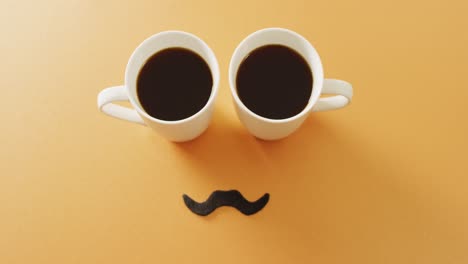 Video-of-two-cups-of-black-coffee-and-false-moustache-on-yellow-background-with-copy-space