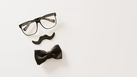 Video-of-black-false-moustache,-glasses-and-bow-tie-on-white-background-with-copy-space