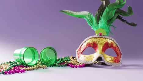 Video-of-carnival-masquerade-mask-with-green-feathers,-mardi-gras-beads-and-shot-glasses