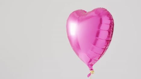Video-of-shiny-pink-heart-shaped-balloon-floating-on-white-background,-with-copy-space