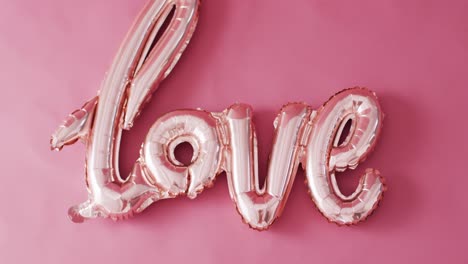 Overhead-video-of-shiny-pale-pink-love-text-balloon,-on-pink-background-with-copy-space