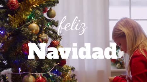 Animation-of-feliz-navidad-christmas-greetings-text-over-caucasian-girl-by-christmas-tree