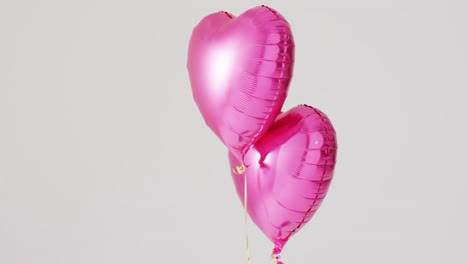 Video-of-two-shiny-pink-heart-shaped-balloons-floating-on-white-background,-with-copy-space