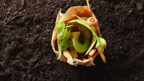 Video-of-bag-of-organic-fruit-and-vegetable-waste-for-composting,-on-dark-soil-with-copy-space