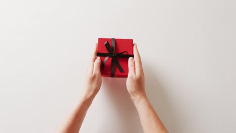 Video-of-hands-placing-red-gift-box-tied-with-black-ribbon-on-white-background,-with-copy-space