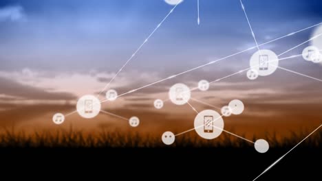Animation-of-network-of-digital-icons-against-landscape-with-grassland-against-sunset-sky