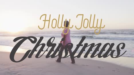 Animation-of-holly-holly-christmas-over-biracial-senior-woman-on-beach