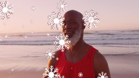 Animation-of-christmas-snow-falling-over-senior-african-american-man-on-beach