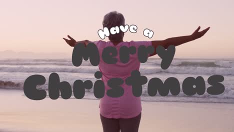 Animation-of-christmas-greetings-text-over-senior-biracial-woman-on-beach