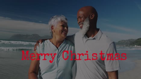 Animation-of-christmas-greetings-text-over-senior-diverse-couple-on-beach