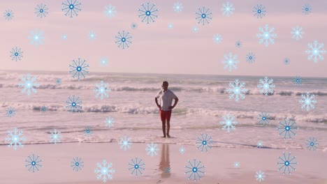 Animation-of-snowflakes-over-african-american-senior-man-on-beach