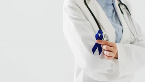 Video-of-midsection-of-caucasian-female-doctor-holding-blue-colon-cancer-ribbon,-with-copy-space