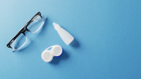 Video-of-pair-of-glasses,-contact-lenses-case-and-solution-on-blue-background-with-copy-space