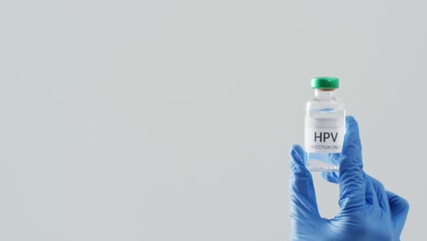 Video-Einer-Hand,-Die-Einen-OP-Handschuh-Trägt-Und-Eine-HPV-Impfstoffflasche-Auf-Grauem-Hintergrund-Mit-Kopierraum-Hält