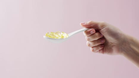 Video-of-holding-white-spoon-of-oil-capsules-on-pink-background-with-copy-space