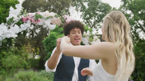 Happy-diverse-couple-dancing-in-garden-on-sunny-day-at-wedding