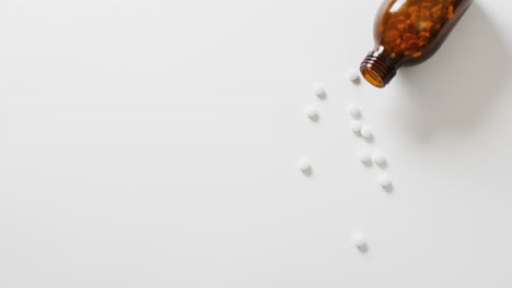Video-of-brown-bottle-spilling-white-pills-on-white-background-with-copy-space