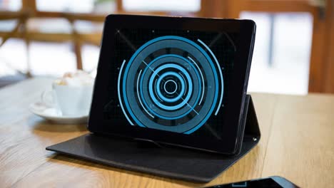 Animation-of-blue-circular-scanner-on-black-screen-of-tablet-on-table-in-cafe