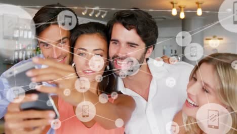 Animation-of-network-of-digital-icons-over-diverse-male-and-female-colleagues-taking-a-selfie-at-bar