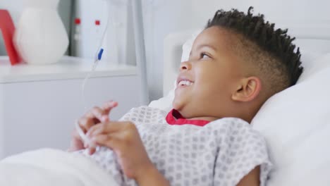 Happy-african-american-boy-patient-lying-in-bed-at-hospital-smiling