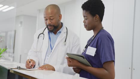 Afroamerikanische-Ärzte-Und-Ärztinnen-Halten-Klemmbrett-Und-Tablet-In-Der-Hand-Und-Reden-Im-Krankenhaus