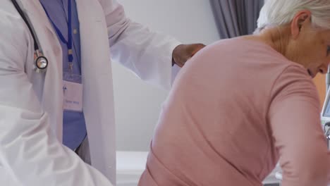 Médico-Varón-Afroamericano-Examinando-La-Espalda-De-Una-Paciente-Caucásica-Mayor-En-El-Hospital