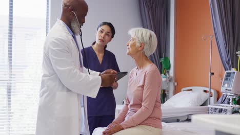 Two-diverse-doctors-examining-senior-caucasian-female-patient-talking-at-hospital