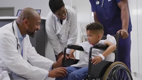Diverse-doctors-talking-to-child-patient-sitting-in-wheelchair-at-hospital