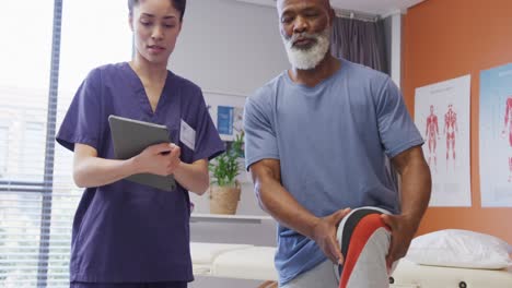 Diverse-female-physiotherapist-and-senior-male-patient-holding-knee-during-physical-therapy-session