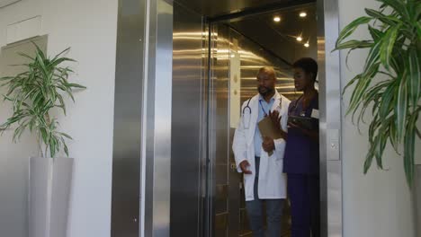 African-american-male-and-female-doctors-holding-clipboard-and-tablet,-talking-at-hospital