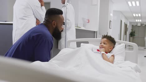 African-american-male-doctor-talking-to-child-patient-laying-in-bed-at-hospital