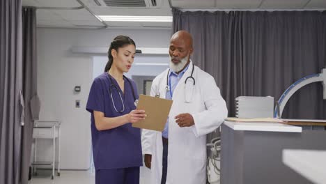 Diverse-male-and-female-doctors-holding-clipboard-in-discussion-at-hospital