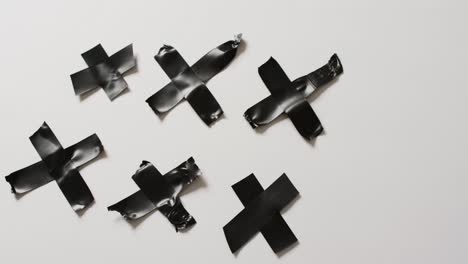 Video-of-close-up-of-black-tape-forming-crosses-on-white-background