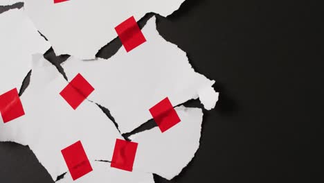 Video-of-close-up-of-torn-pieces-of-white-paper-with-red-tape-on-black-background