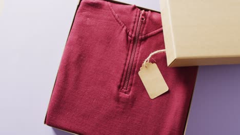 Video-of-close-up-of-red-sweater-with-tag-in-box-on-purple-background