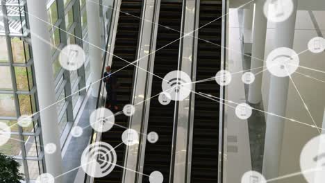 Animation-of-network-of-digital-icons-over-businessman-on-escalator-at-modern-office
